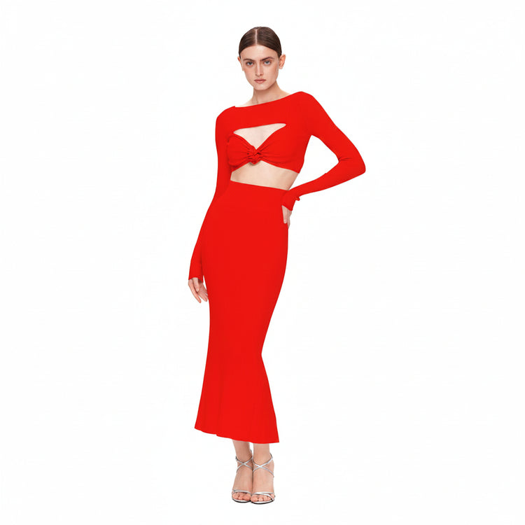 A woman modeling a bright red two-piece dress set against a plain white background. The set features a long-sleeve crop top with a twisted front detail and a matching high-waisted, flared maxi skirt.