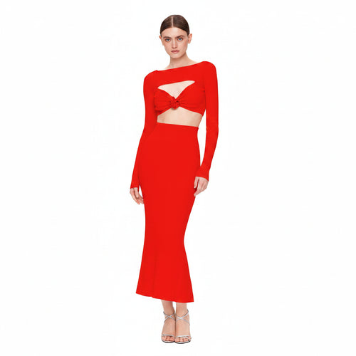 A woman modeling a bright red two-piece dress set against a plain white background. The set features a long-sleeve crop top with a twisted front detail and a matching high-waisted, flared maxi skirt.