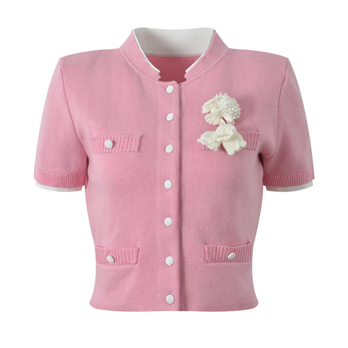 Pink cardigan with white buttons and a decorative flower on a white background