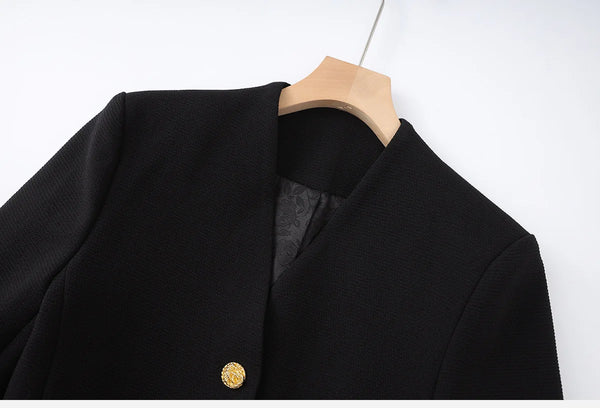 Black coat with a gold button on a wooden hanger against a white background