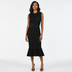 A woman modeling a sleeveless black midi dress with textured horizontal knit lines, a studded waistband, and a ruffled hem, set against a plain white studio background.