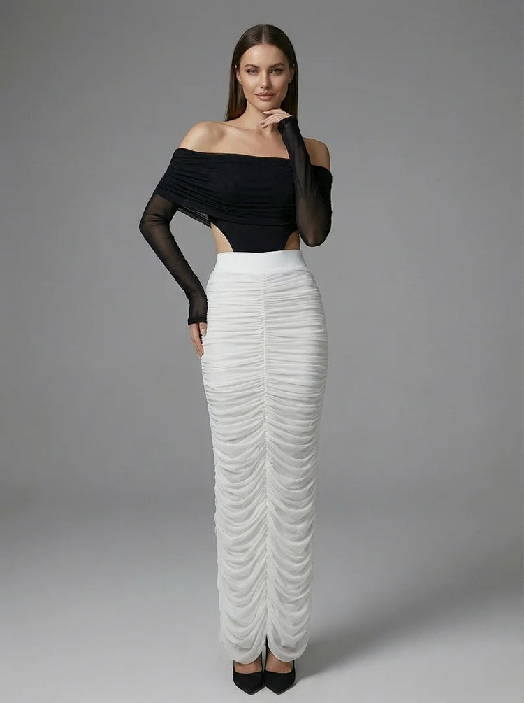 Woman wearing a black off-shoulder top and white ruched skirt on a gray background