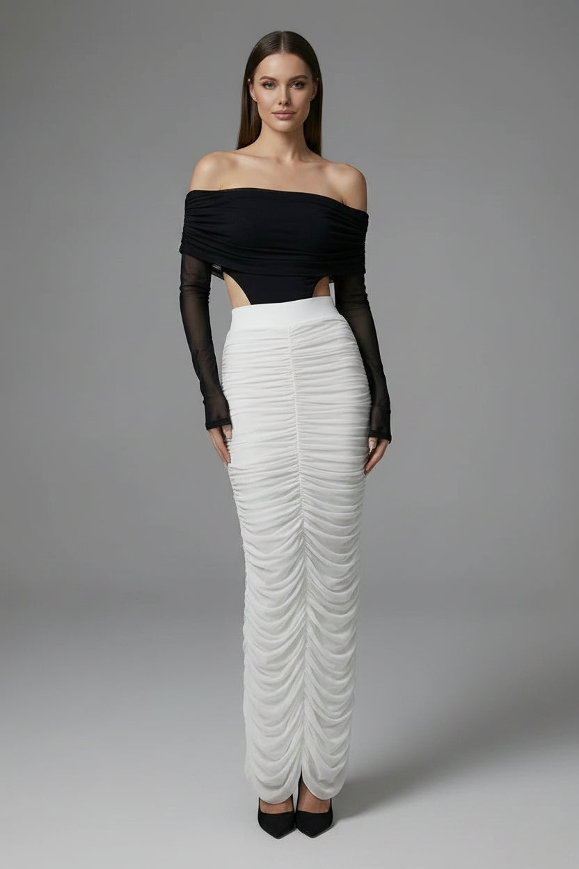 Woman wearing a black off-shoulder top and white ruched skirt on a gray background