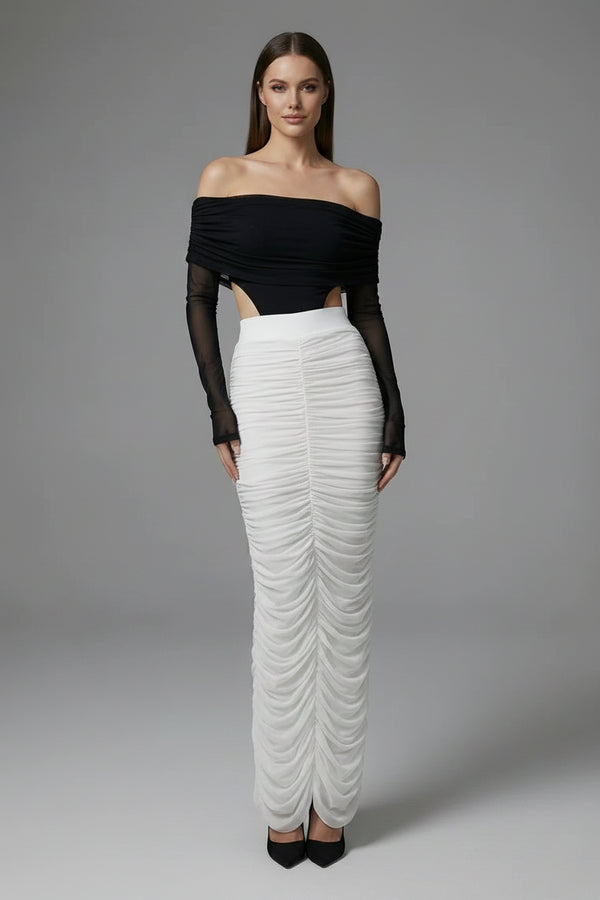 Woman wearing a black off-shoulder top and white ruched skirt on a gray background