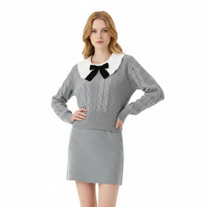 Woman wearing a gray sweater dress with a white collar and black bow tie on a white background