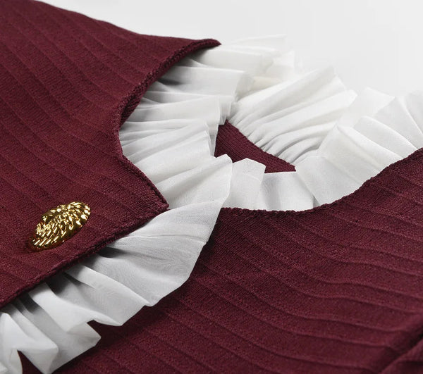 Close-up of a maroon garment with white ruffles and a gold button on a white background