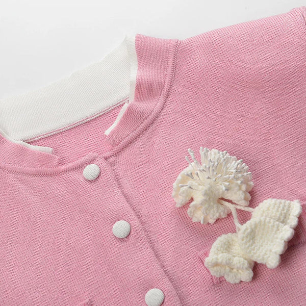 Close-up of a pink baby outfit with white buttons and floral details on a light gray background