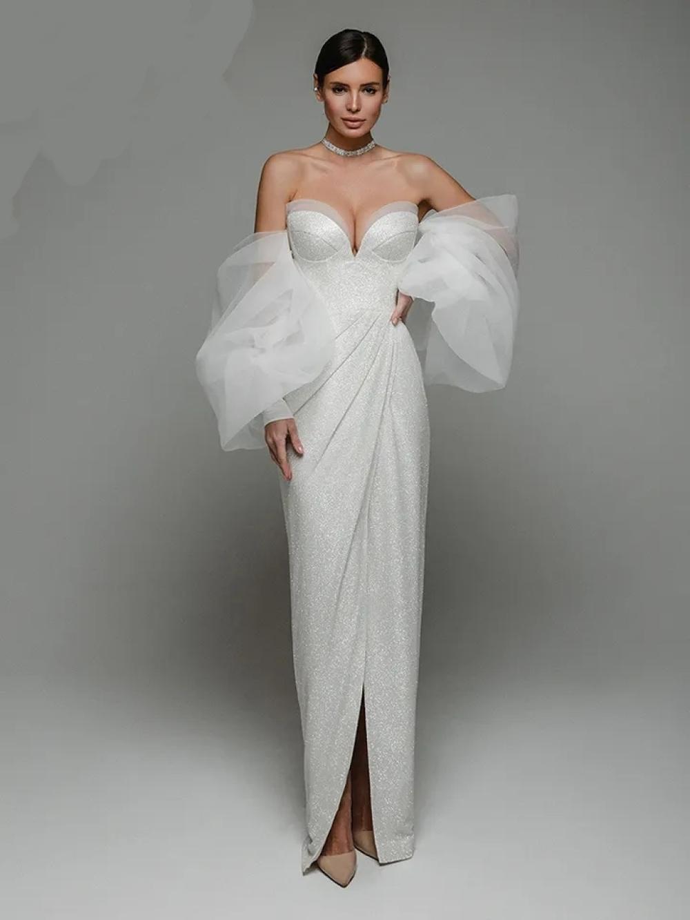 Woman wearing a white strapless gown with large sleeves on a plain background