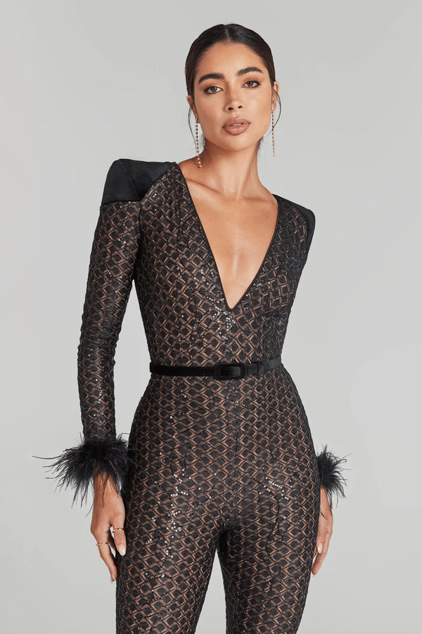 Woman wearing a black lace jumpsuit with feathered sleeves on a gray background