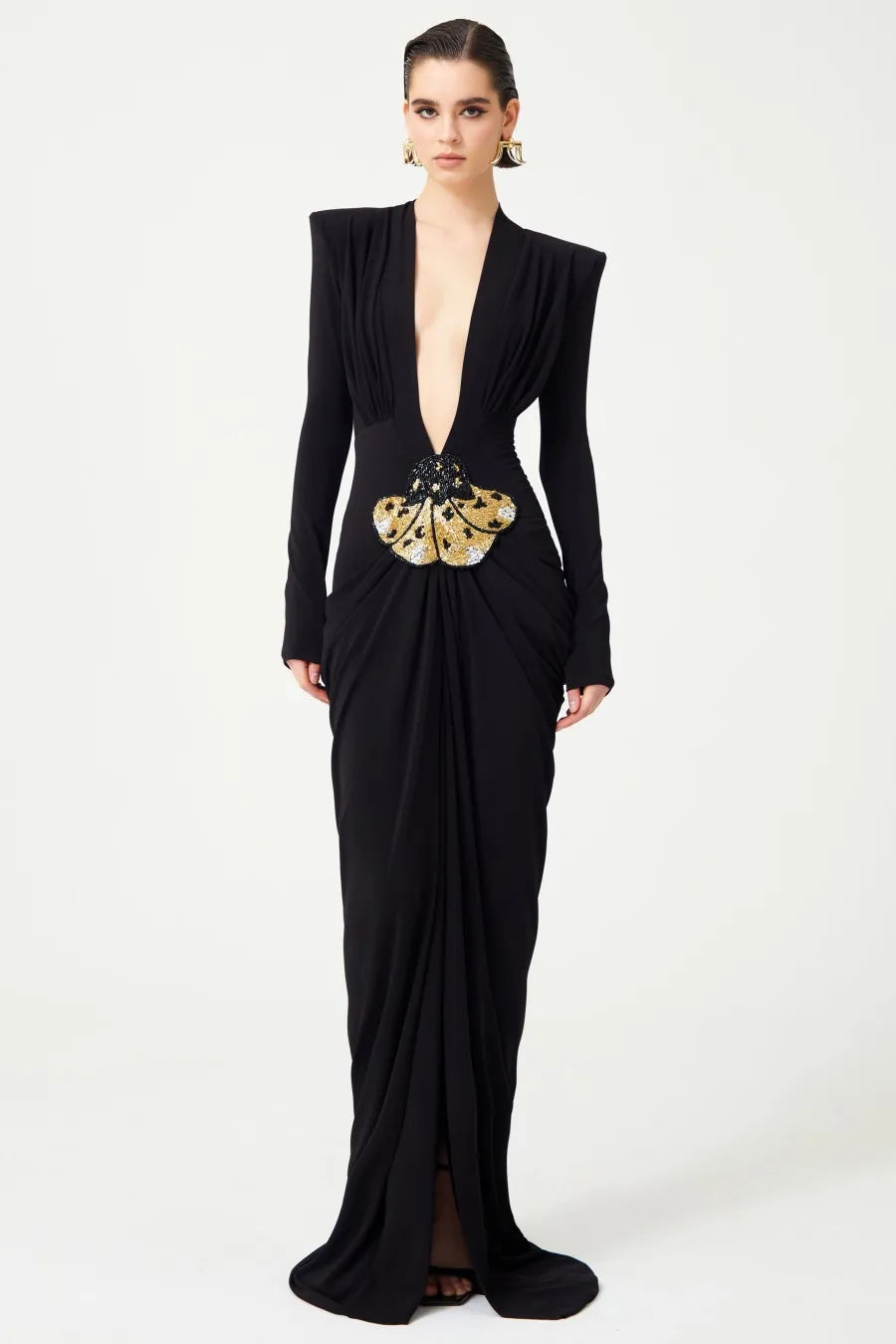 A woman wearing a deep V-neck, bodycon maxi dress with long sleeves and a decorative belt at the waist.