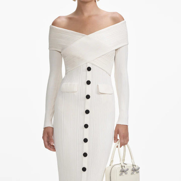 White off-shoulder dress with black buttons and a handbag on a white background