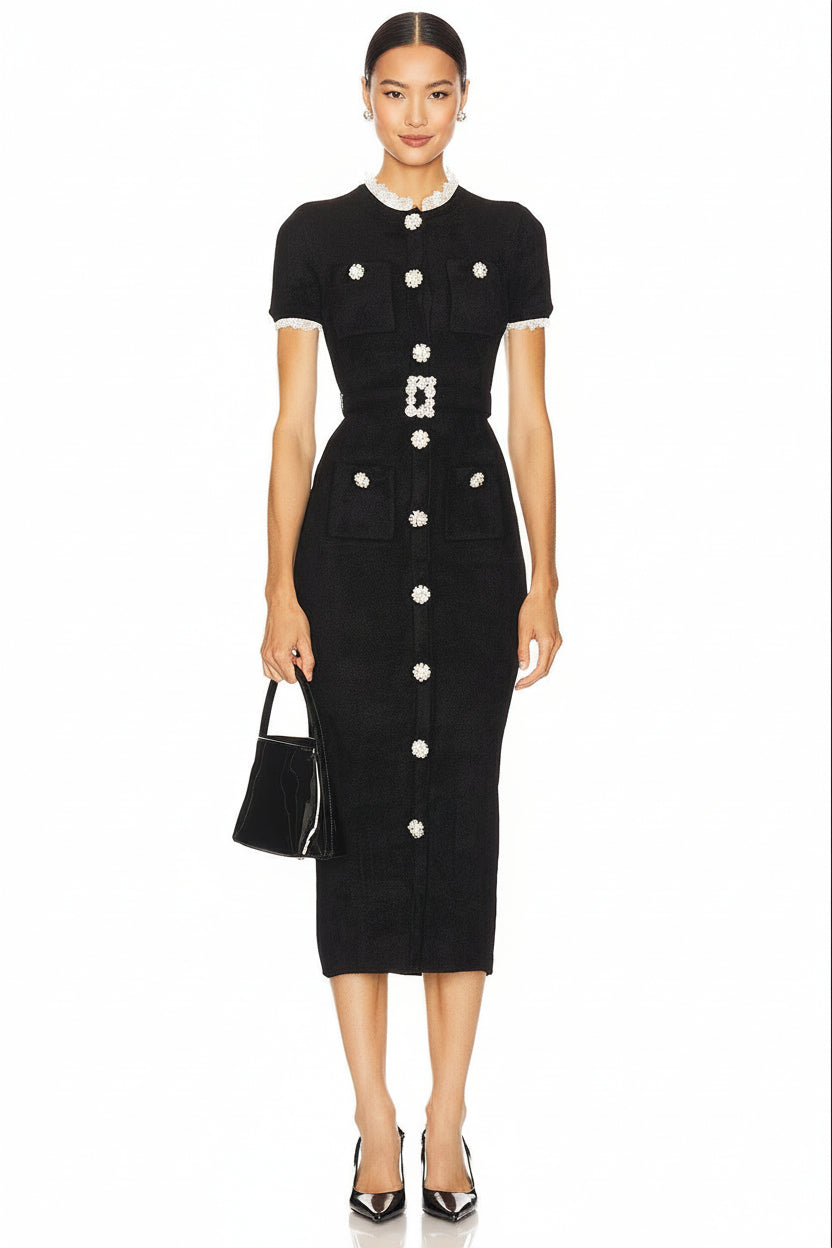 A model wearing a black short-sleeve midi dress with white trim and prominent white decorative buttons, holding a small black handbag against a plain white background.