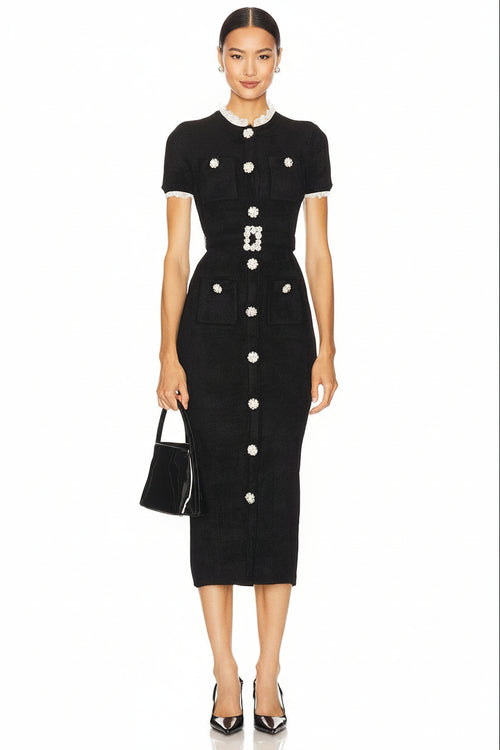 A model wearing a black short-sleeve midi dress with white trim and prominent white decorative buttons, holding a small black handbag against a plain white background.