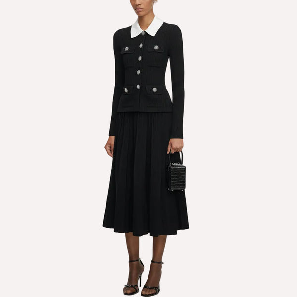 Woman wearing a black outfit with a white collar, holding a black handbag on a white background