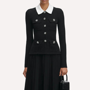 Black ribbed sweater with white collar and decorative buttons on a plain background
