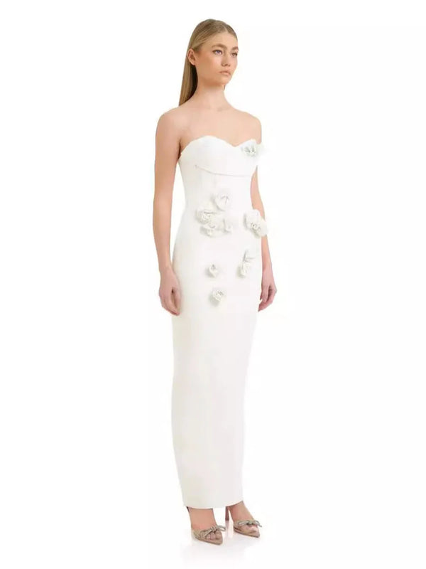 Woman wearing a strapless white evening gown with floral embellishments on a white background
