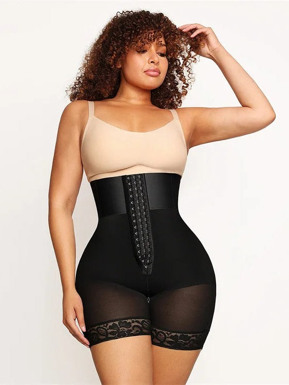 A woman modeling a black high-waisted shapewear brief with lace trim and a lace-up front closure, worn over a beige camisole against a plain light background.
